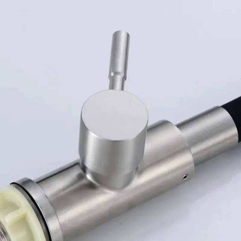 A close-up of a brushed stainless steel mechanical component with a cylindrical body, a vertical cylindrical protrusion, and a black cable or hose section on the right, photographed on a light gray background.