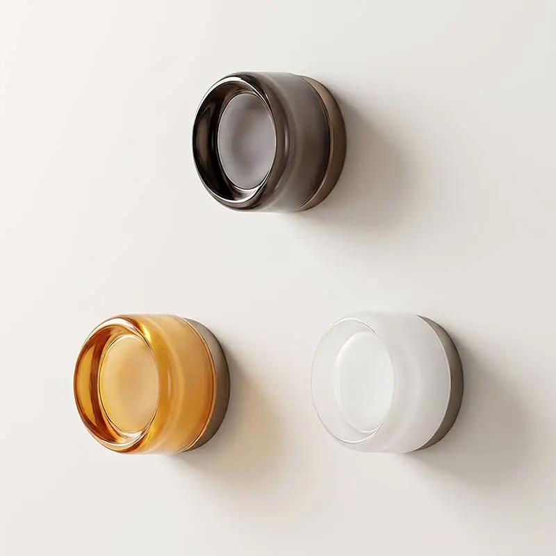 Minimalist Glass Wall Light, three circular glass fixtures in amber, smoky and clear finishes mounted on a pale wall.
