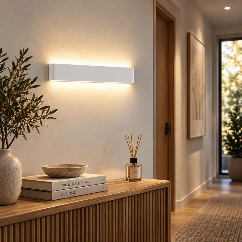 A modern rectangular wall sconce with a matte white finish, mounted on a beige wall in a warm, contemporary hallway setting.