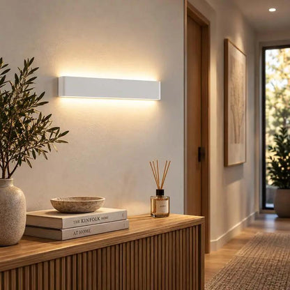 A modern rectangular wall sconce with a matte white finish, mounted on a beige wall in a warm, contemporary hallway setting.