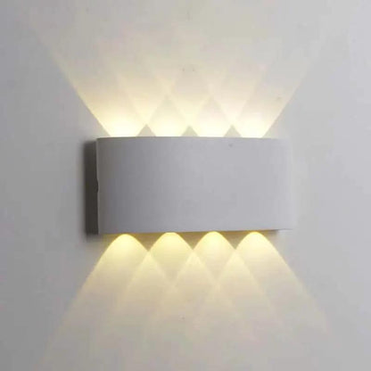 A modern rectangular wall sconce light fixture mounted on a white wall, casting warm light upward and downward in a diamond pattern.