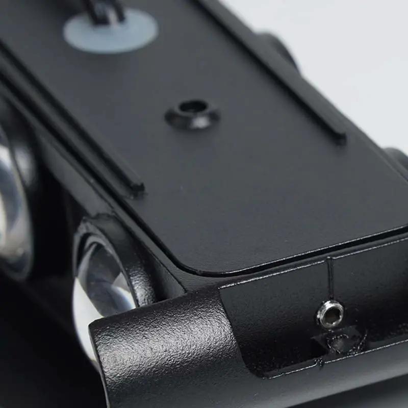 Close-up of a black metal camera accessory or mount with screws, ridges, and part of a lens visible, photographed on a light neutral background.