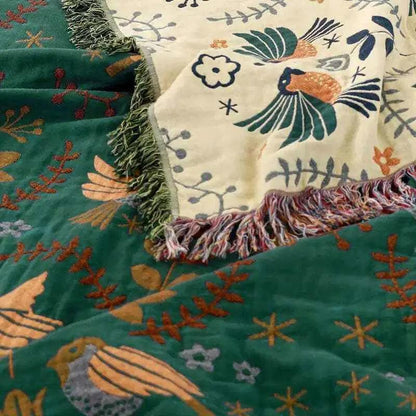100% Cotton Reversible Throw Blanket draped over green and cream bird-pattern throws with fringe; decorative for sofa or bed.