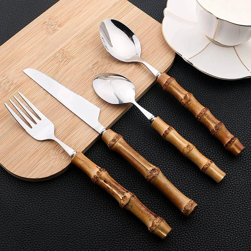 24-Piece Bamboo Handle Cutlery Set - Stainless Steel Flatware; bamboo-handled utensils on a board beside plates.