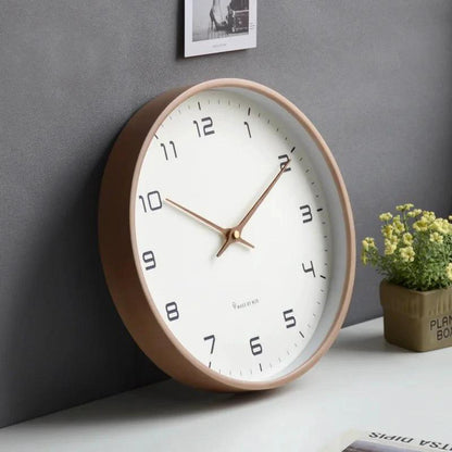 Nordic Wooden Wall Clock with white dial and copper hands, shown on a desk against a grey wall in a minimalist room.