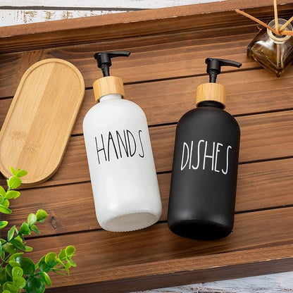 Two soap dispensers labeled 'HANDS' and 'DISHES' on a wooden surface with a wooden tray and plant in the background.