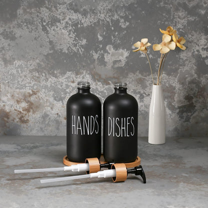 Black 'HANDS' and 'DISHES' bottles with a white vase with flowers on a textured gray background